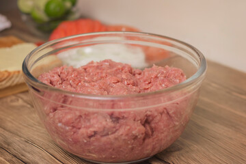 glass bowl with minced raw beef or beef pork on wooden table in the comfort of home