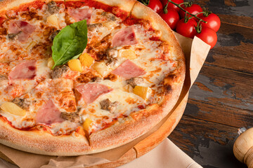 Pizza with ham and pineapples, on a wooden background with basil