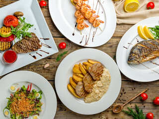 Pork medallions with fries, dorado on grill, shrimps skewers, steak from beef and salad top view on wooden table