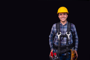 Young man smiling with his tools and safety equipment, on an isolated black background, copy paste, concept of safety at work