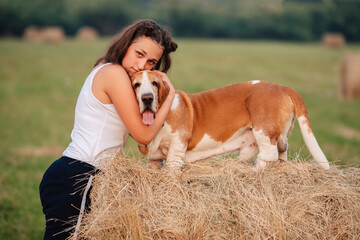 A young adult girl walks with a Basset Hound dog in nature. The owner hugs the pet.