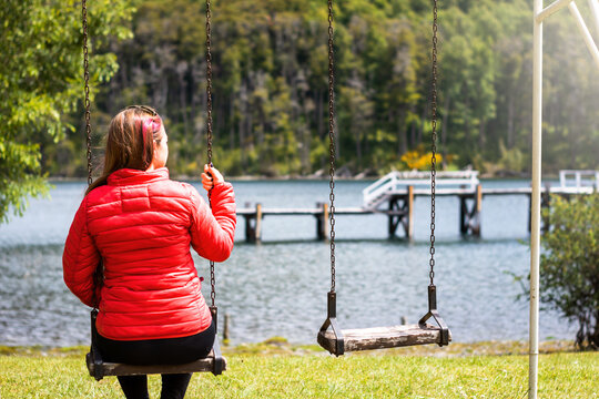 Mujer sentada en amacas mirando muelle de lago patag&oacute;nco, en cercan&iacute;as de San Mart&iacute;n de los Andes