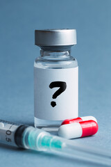 A question mark on a mysterious vial containing a vaccine next to a syringe and some red and white pills