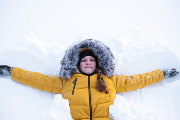 Fototapeta na wymiar A girl in a yellow down jacket with a hood is lying on the snow