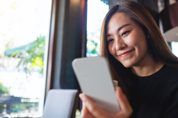 Closeup of a young woman holding and using mobile phone while drinking coffee in cafe