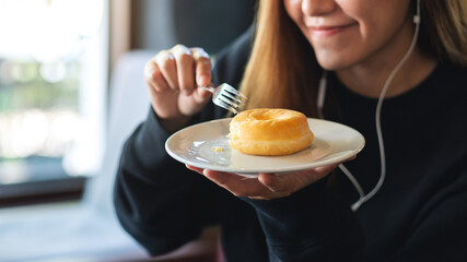 Closeup of a young woman with earphones holding and eating donut