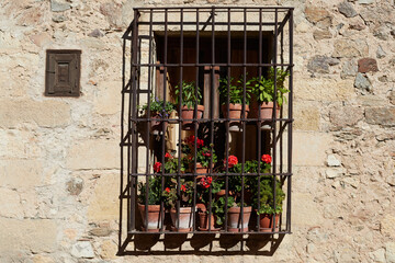 Fototapeta na wymiar Window with railings and flower pots in a stone house