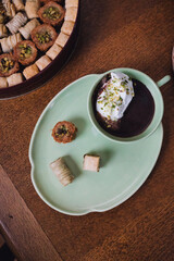 drinking chocolate in matching green cup and plate with assorted baklava desserts on wood table