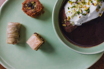 close up drinking chocolate in matching green cup and plate with assorted baklava desserts