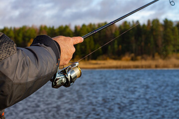 Hand with a fishing rod. Fisherman with a fishing rod. Close-up is a hand holding a spinning rod. Colorful view, blurred background, selective focus.