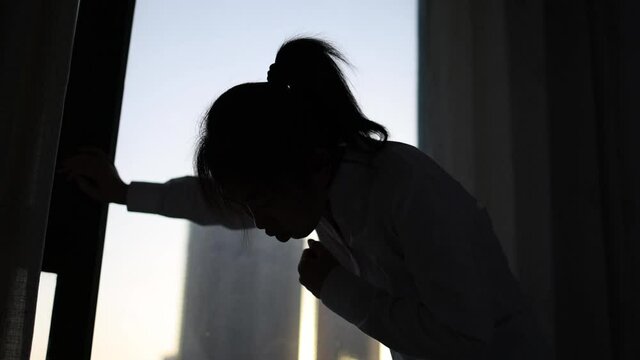 Silhouette of a woman coughing and panting at the window.