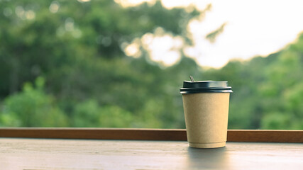 Disposable coffee cup on wooden table with nature background.