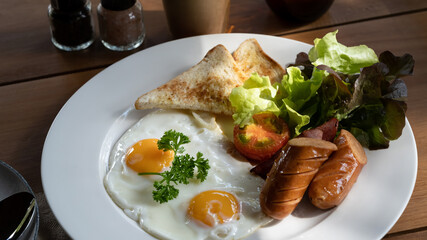 English breakfast with fried eggs, bacon, sausages, toasts and fresh salad.