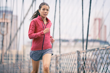 Sports athlete woman runner running on Brooklyn Bridge, New York City. Asian girl training outdoor...