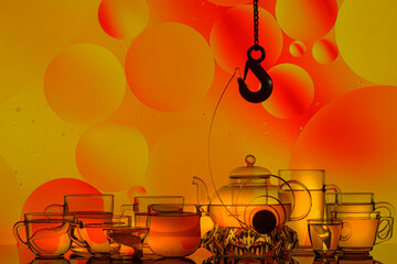 transparent glass teapot and cups with tea and drops, silhouette of lifting hook on colorful background 