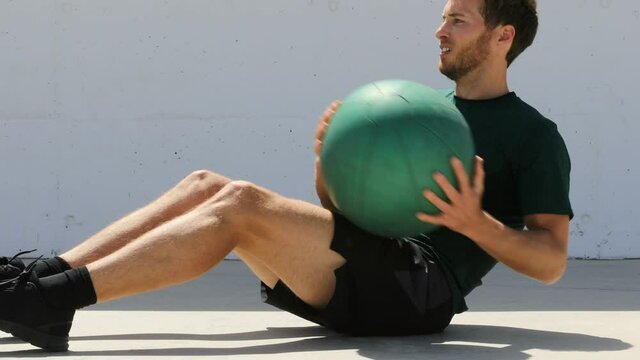 Medicine ball exercise. Mandoing russian twist abs workout. Fitness athlete working out doing strength training crunches oblique muscles with equipment on gym floor outdoors