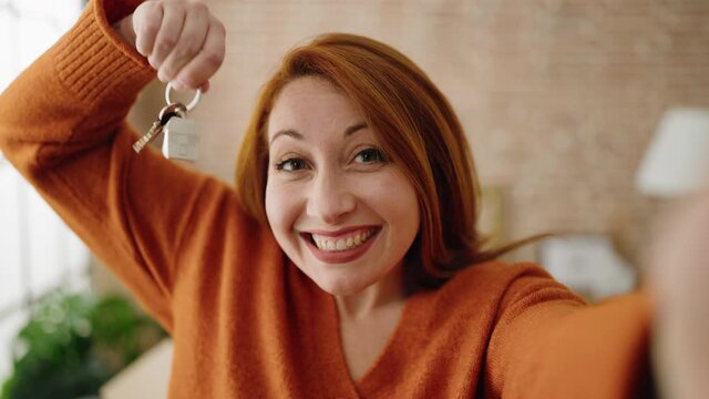 Young redhead woman having video call holding key of new house at new home