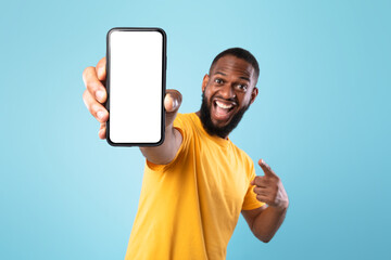 Mobile app advertisement. Excited black man pointing at smartphone with empty screen, mockup. Space...