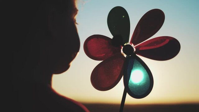 kid pinwheel. little baby girl silhouette play with windmill toy wind in the park. happy family kid dream concept. baby girl play toy fun pinwheel the glare sunset of the sun at in the park