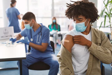 Black Guy Showing Vaccinated Arm With Adhesive Bandage In Clinic