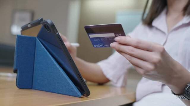 Close up female hand holding a mock up credit card showing a CVV security on backside of card, with other hand writing a wireless smart pen on tablet screen, people and convenience banking technology