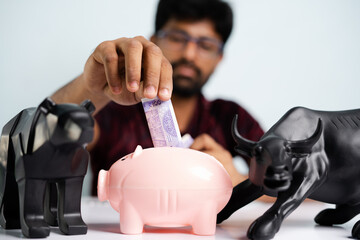 focus on money, Close up shot of Young man placing money inside the piggy bank - concpet of savings, investment in equity or mutual fund stocks. - obrazy, fototapety, plakaty