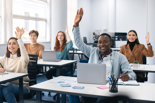 Portrait of diverse students raising hands at modern classroom