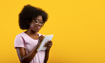 Smart african american female student in glasses writing checklist, taking notes in copybook over...