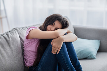 Unhappy teen girl feeling depressed or desperate, sitting on couch at home, suffering from problem...