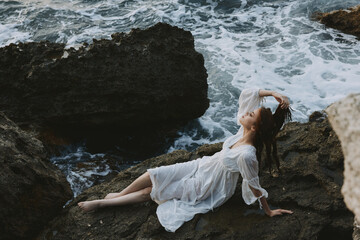 A woman in a white dress barefoot lies on a stone hold by her hair