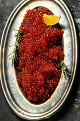 Red caviar in metal plate and a glass of champagne on a stone background. Gourmet food close up, appetizer, selective focus, place for text