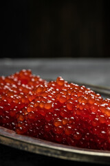 Red caviar in metal plate on dark background. Gourmet food close up, appetizer, selective focus, place for text