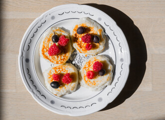Cottage cheese pancakes on ceramic plate with fresh raspberries and gooseberries. Top view of gourmet breakfast.