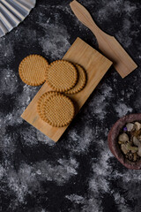 Five cinnamon cookies, on a wooden board and a kitchen utensil, on a dark background, with gray and white spots.