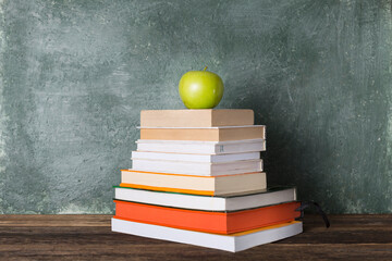 A stack of books and a green apple on the background of the school board. Education and back to school concept.
