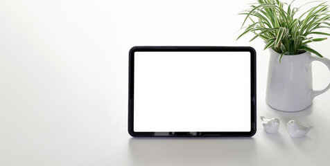 Mockup blank white screen portable tablet and houseplant on white table with copy space.