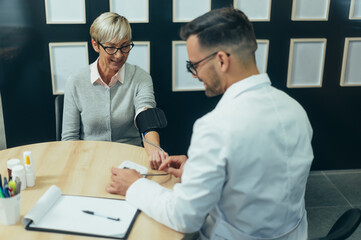 Obraz premium Smiling senior woman patient in doctor's office checking blood pressure