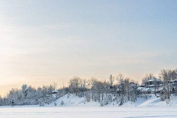 Old russian village houses and winter trees on the shore of a snowy lake