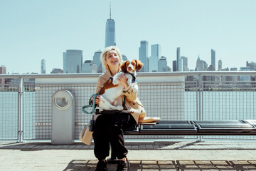 Young stylish woman walking puppy dog in the city with skyline background.