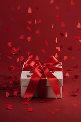 Presents with red bow on red background with heart confetti. Flat lay style. Valentine day concept. Saint Valentines
