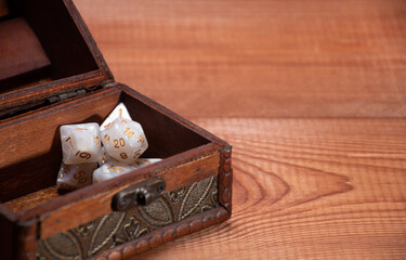 Selective focus on set of role playing white dices lie in storage box on gaming table made of wood, banner: concept for role-playing games with place for text, crop, side view