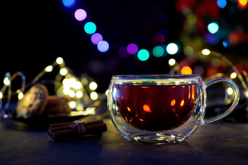 Transparent cup with black tea on blurred holiday lights background