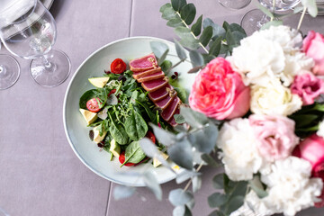 Fototapeta na wymiar tuna salad on the serving table with wine glasses and flowers. grey tablewear. selective focus