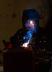 A welder in a workshop with a welding machine, welds metal structures. A worker in a factory uses a...