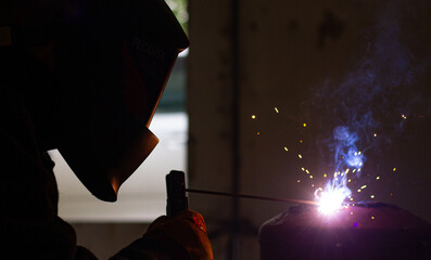 A welder in a workshop with a welding machine, welds metal structures. A worker in a factory uses a...