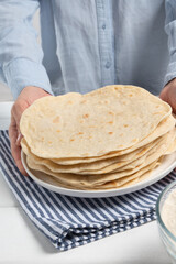 Human puts in Indian bread (roti) on white wooden table. Obscured face. Close-up.
