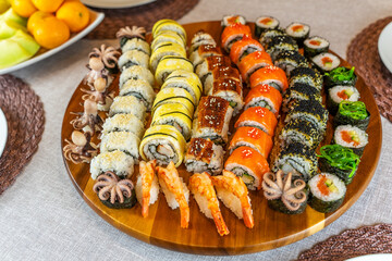 Assortment of rolls and sushi on a wooden board on a festive table. Rolls with salmon, shrimps, omelette, octopus, crab, unagi. 