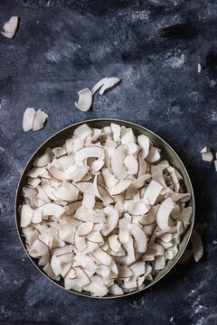 healthy snack: home made roasted coconuts chips in black bowl on dark background. Vegan. Clean eating. Plant based.
