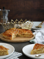 A piece of traditional French galette des rois with paper crown, plate and cutlery. Cake made with...