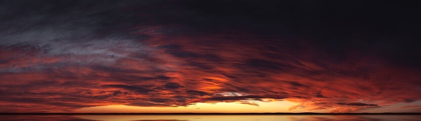 Fototapeta na wymiar Sunset from bright saturated clouds. Dramatic sunset-sunrise with a pronounced texture of clouds and reflections on the horizon. Panorama of the evening sky with rich contrast of colors